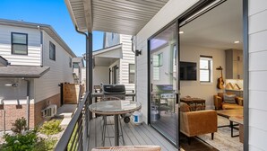 A modern patio with a glass door leading to a living area, featuring a grill, seating, and a guitar.
