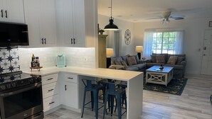 A modern kitchen with white cabinets, a built-in oven, and a dining area with blue bar stools. - Swim Up Bar - Outdoor Paradise! (Delray Beach)