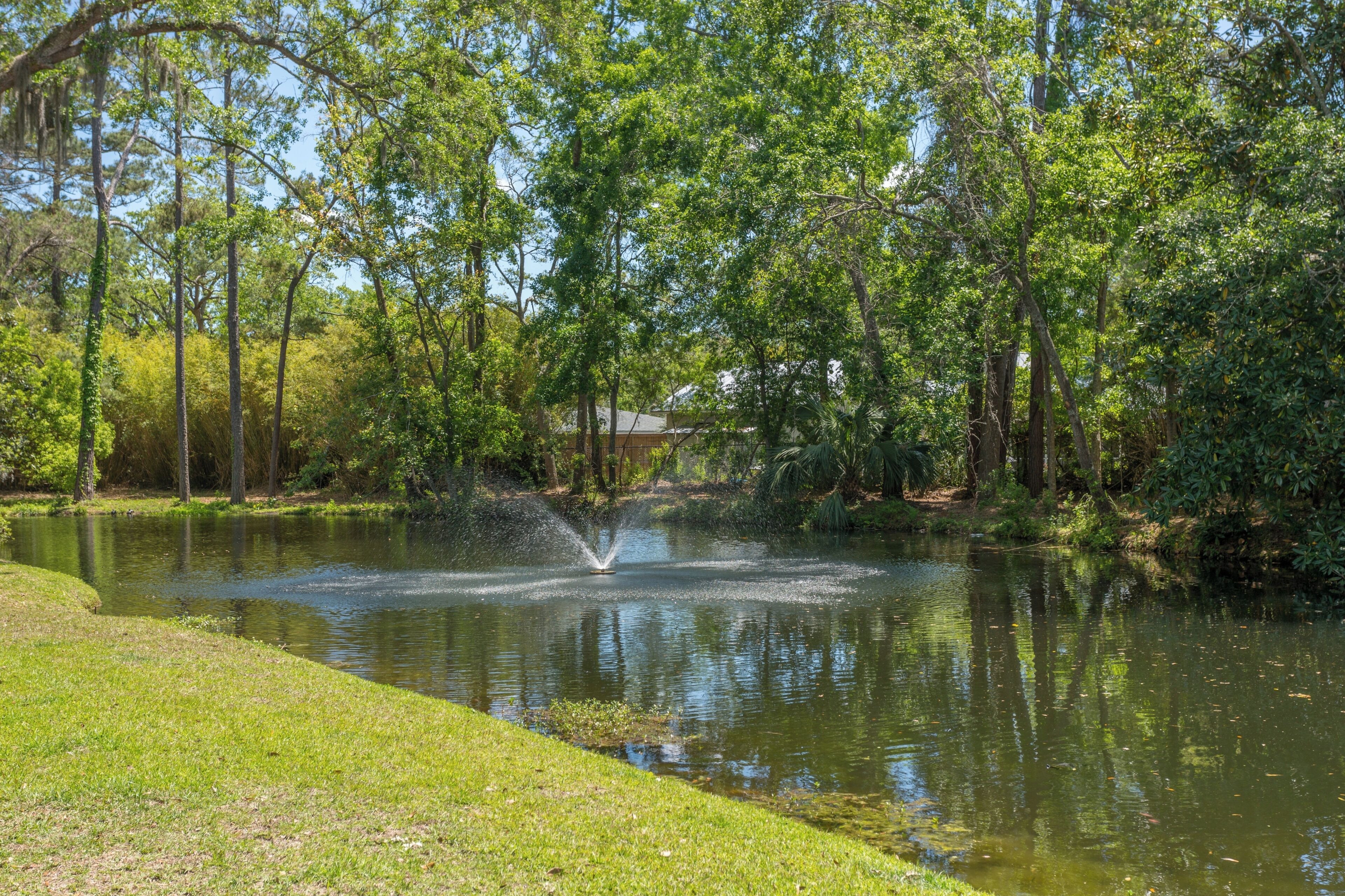 Un étang avec une fontaine, entouré d’arbres et bordé d’une pelouse.