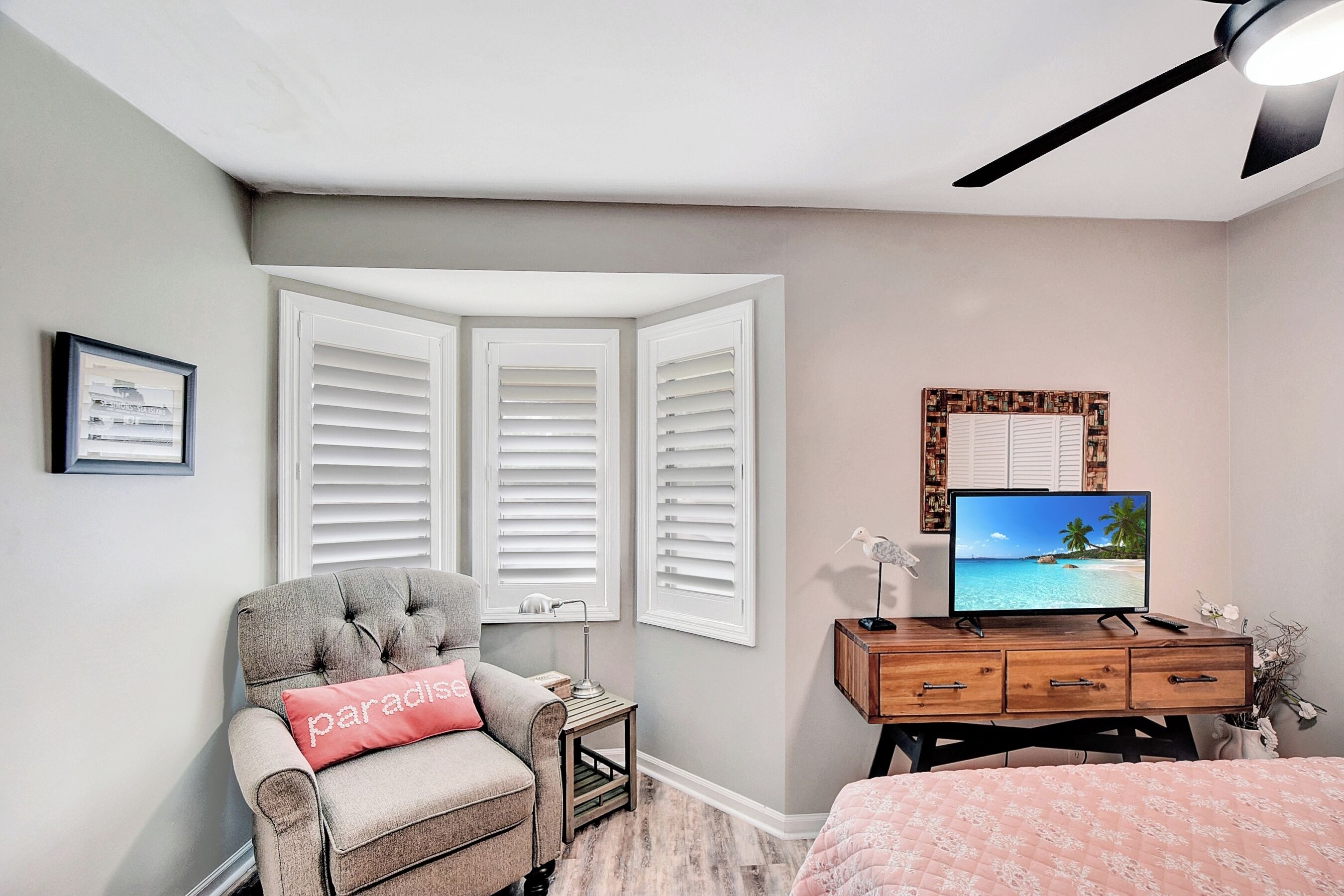 Une chambre à coucher avec un fauteuil à capitons, un bureau avec une télévision et un lit recouvert d’une couette rose.