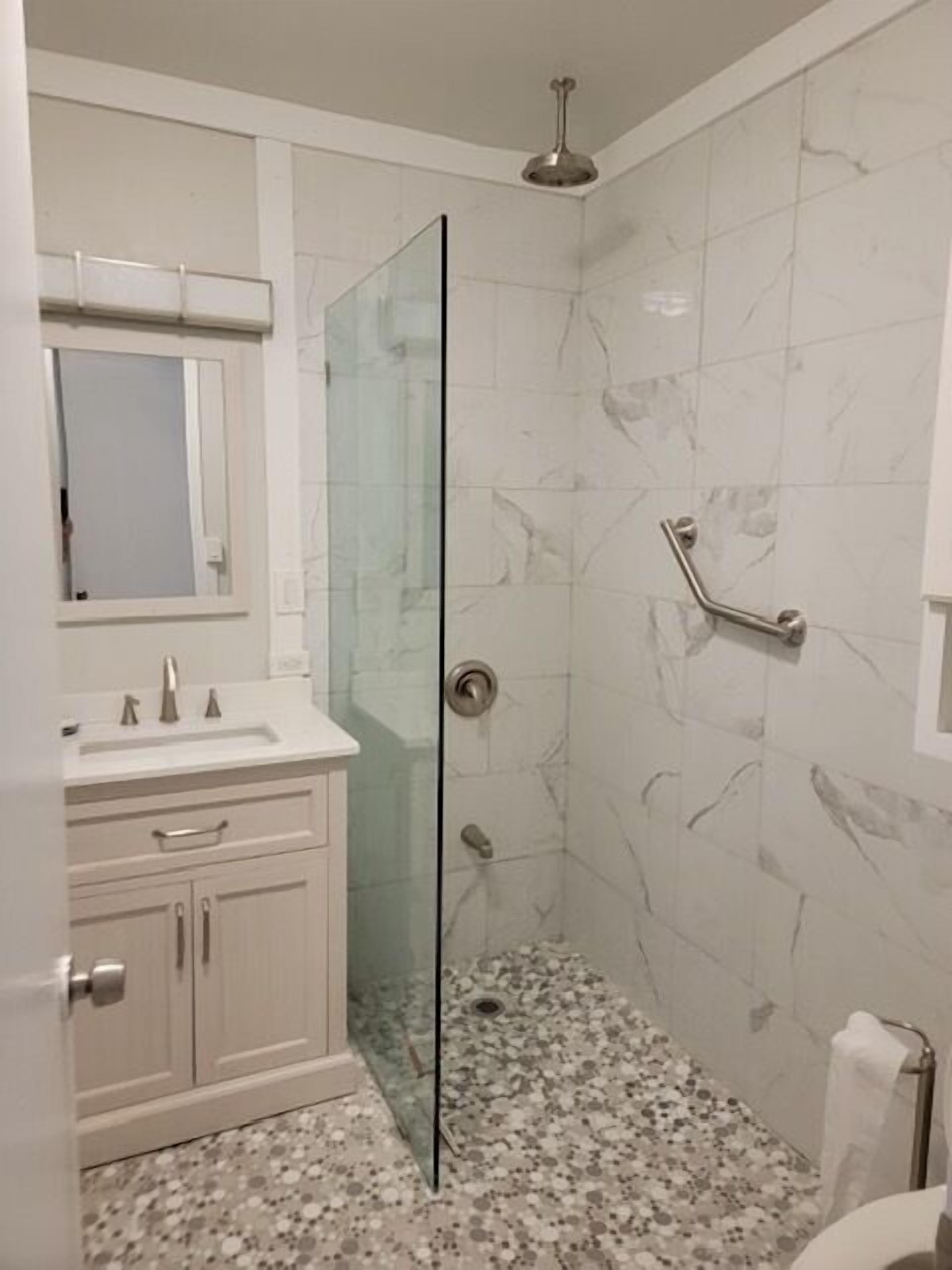 Une salle de bain avec une douche à parois de verre, des carreaux de marbre, un meuble-lavabo blanc et des toilettes.
