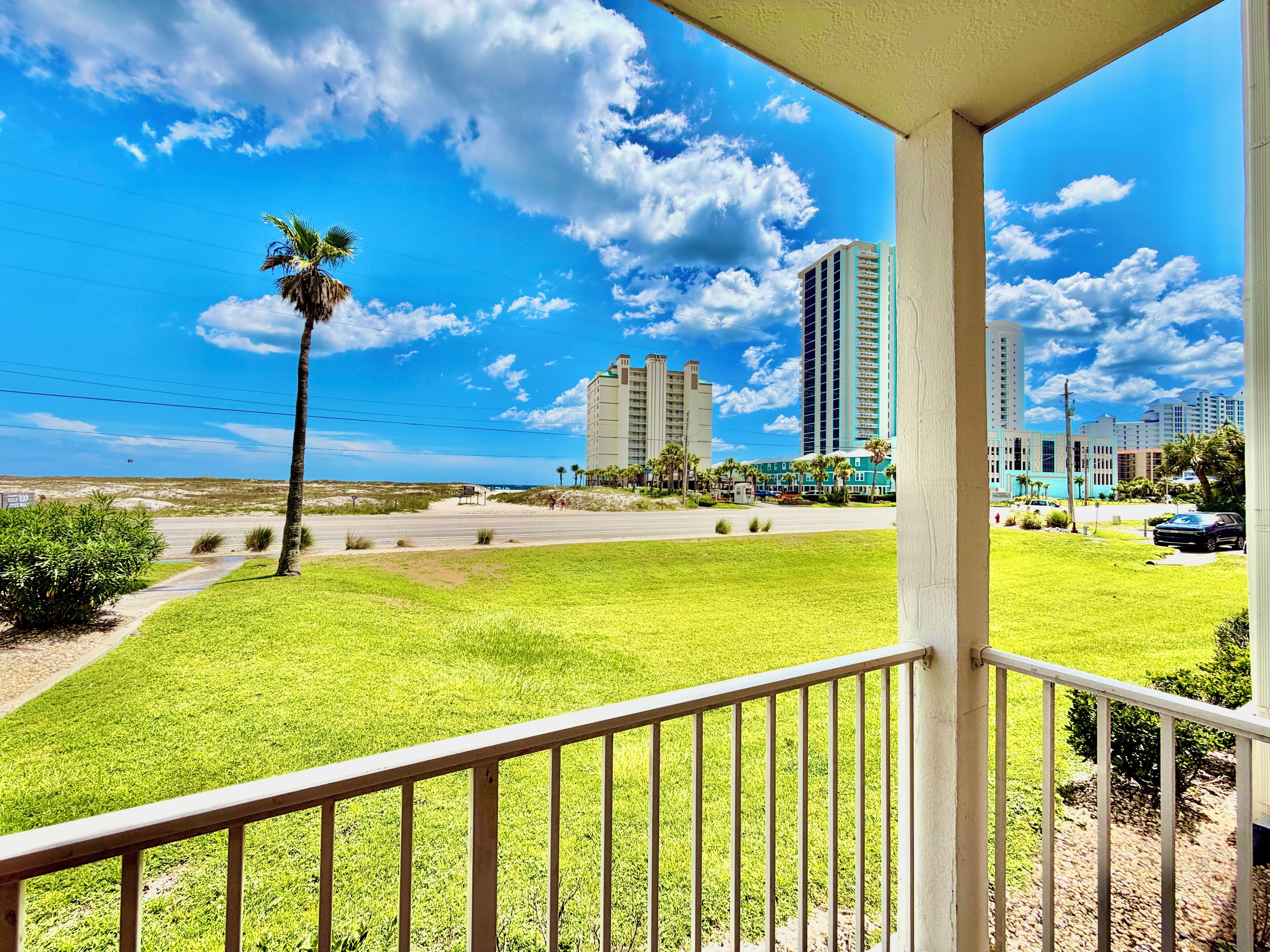 A balcony with a view of a grassy area, a palm tree, and a cityscape with tall buildings.