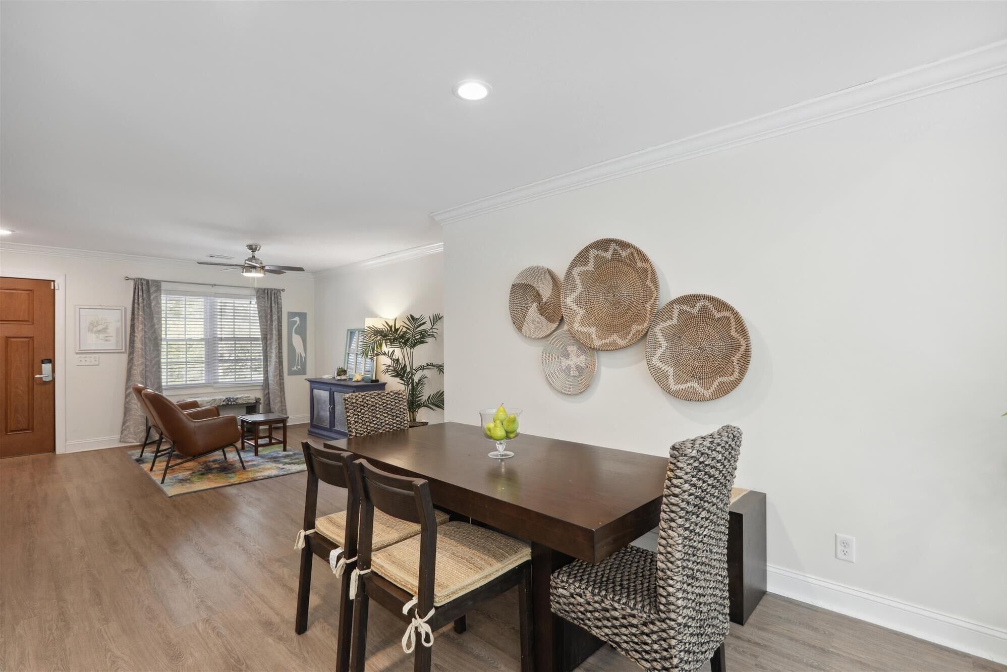A dining area with a wooden table and chairs, a ceiling fan, and wall-mounted woven art pieces.