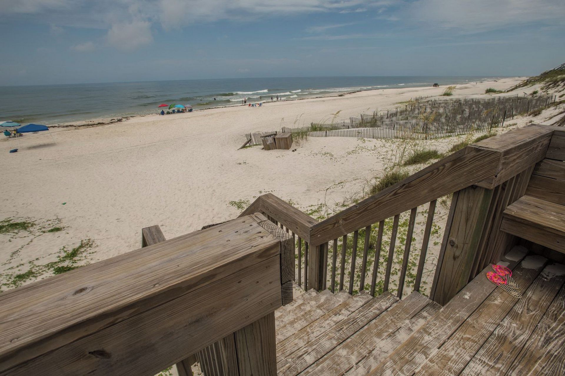 A beach with a wooden boardwalk leading to the shore, a sandy beach, and the ocean in the background.