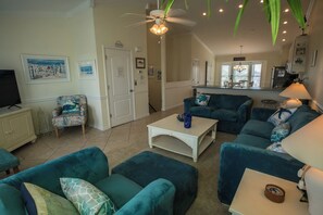 A spacious living room with teal sofas, a white coffee table, and a ceiling fan.
