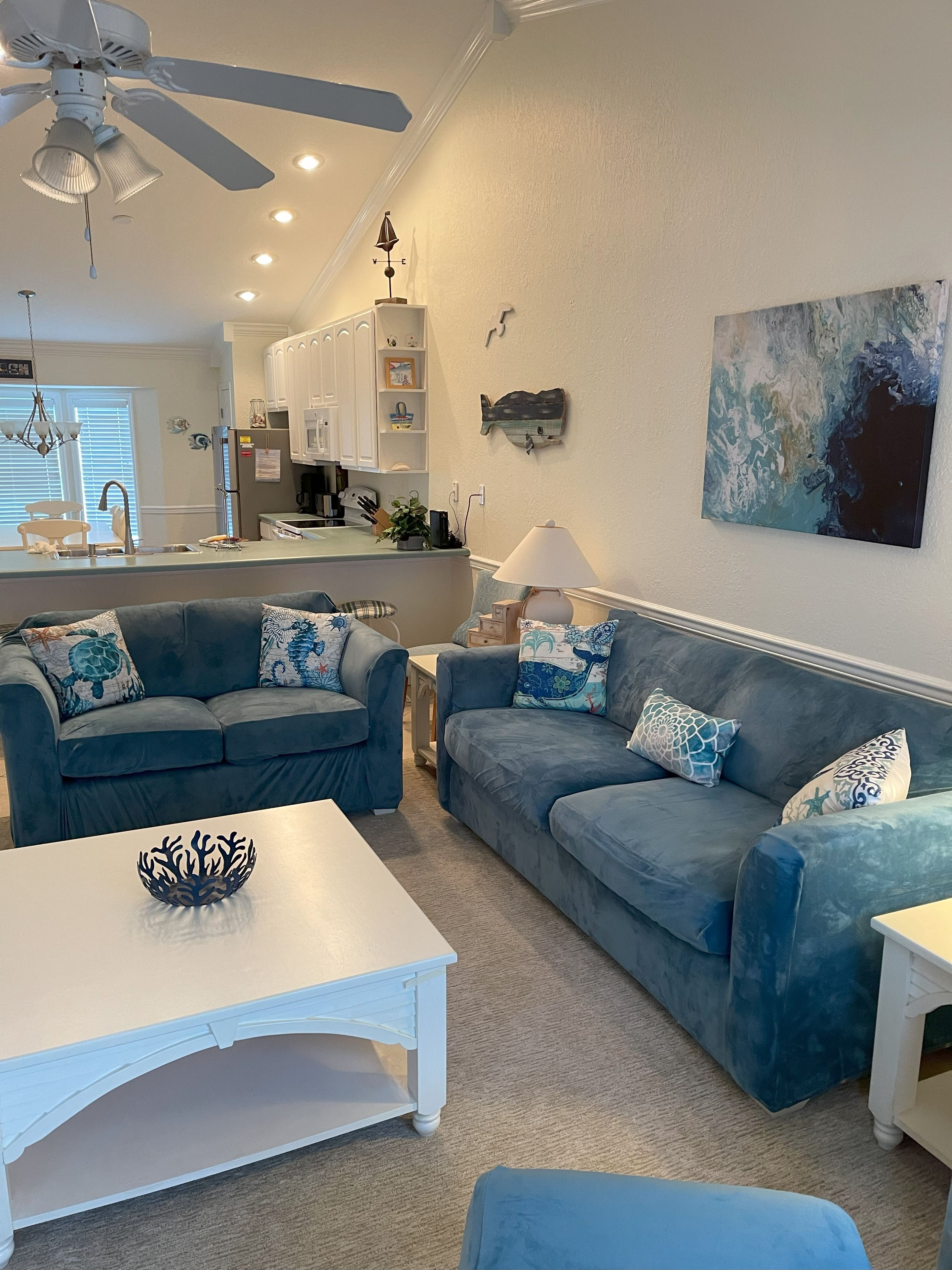 A living room with a blue sofa set, a white coffee table, and a ceiling fan.