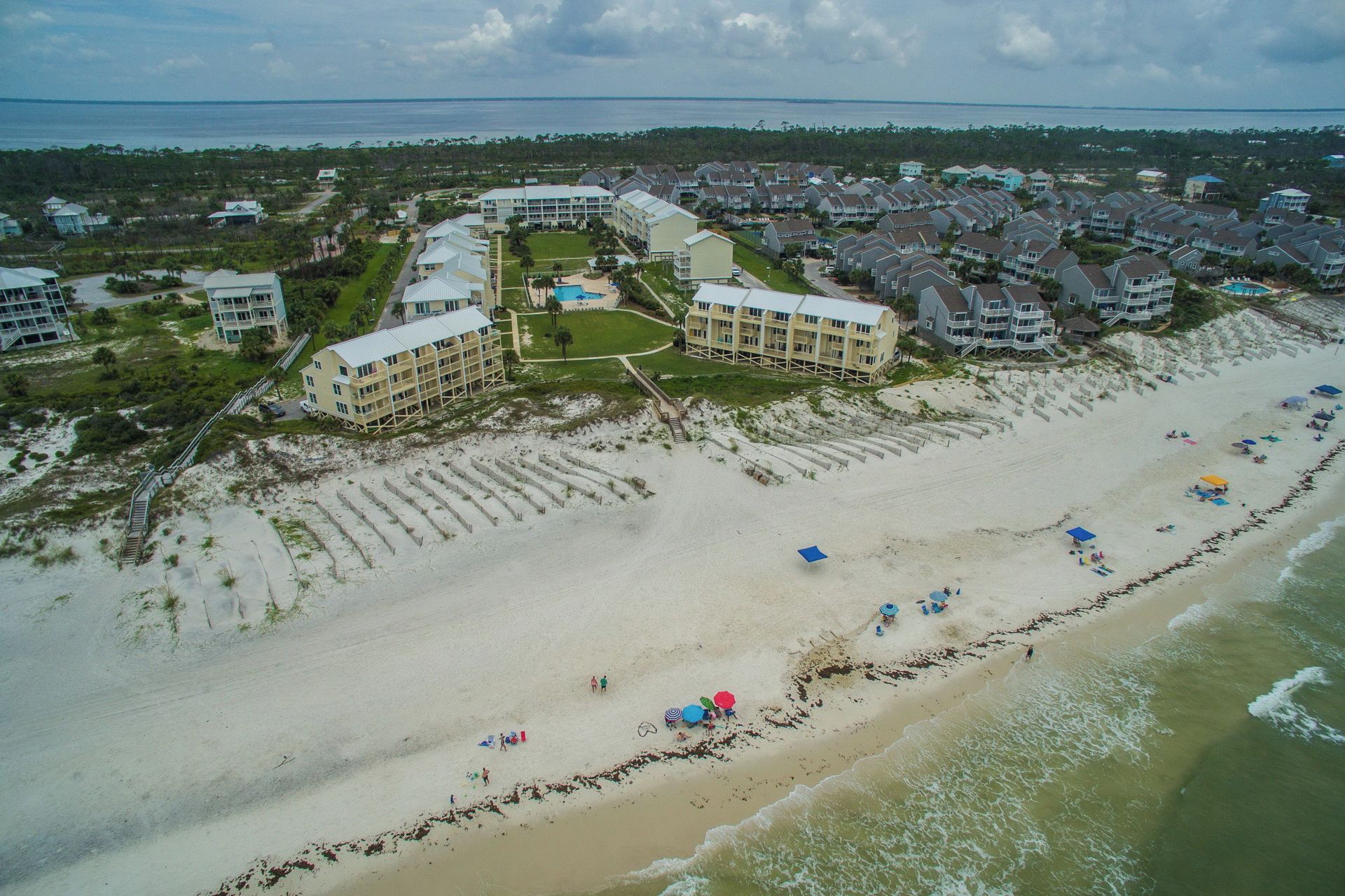 An aerial view of a coastal resort with multiple buildings, a sandy beach, and a clear view of the ocean.
