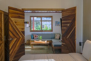 A room with a wooden partition, a sofa, a coffee table, and a window with a view of greenery.
