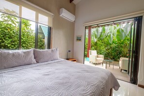 Ein Schlafzimmer mit einem großen Bett, einem Fenster, einer Klimaanlage, einem kleinen Tisch und einem Stuhl.