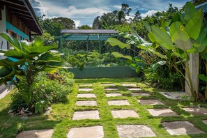 A garden with a stone pathway, lush greenery, and a greenhouse structure.