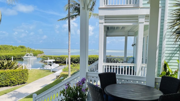A covered outdoor area with a view of the sea, a boat docked nearby, and a table with chairs. - Spectacular Ocean Front Home In Beautiful Islamorada!Slip,Com Pool, & Prv Bch (Islamorada)