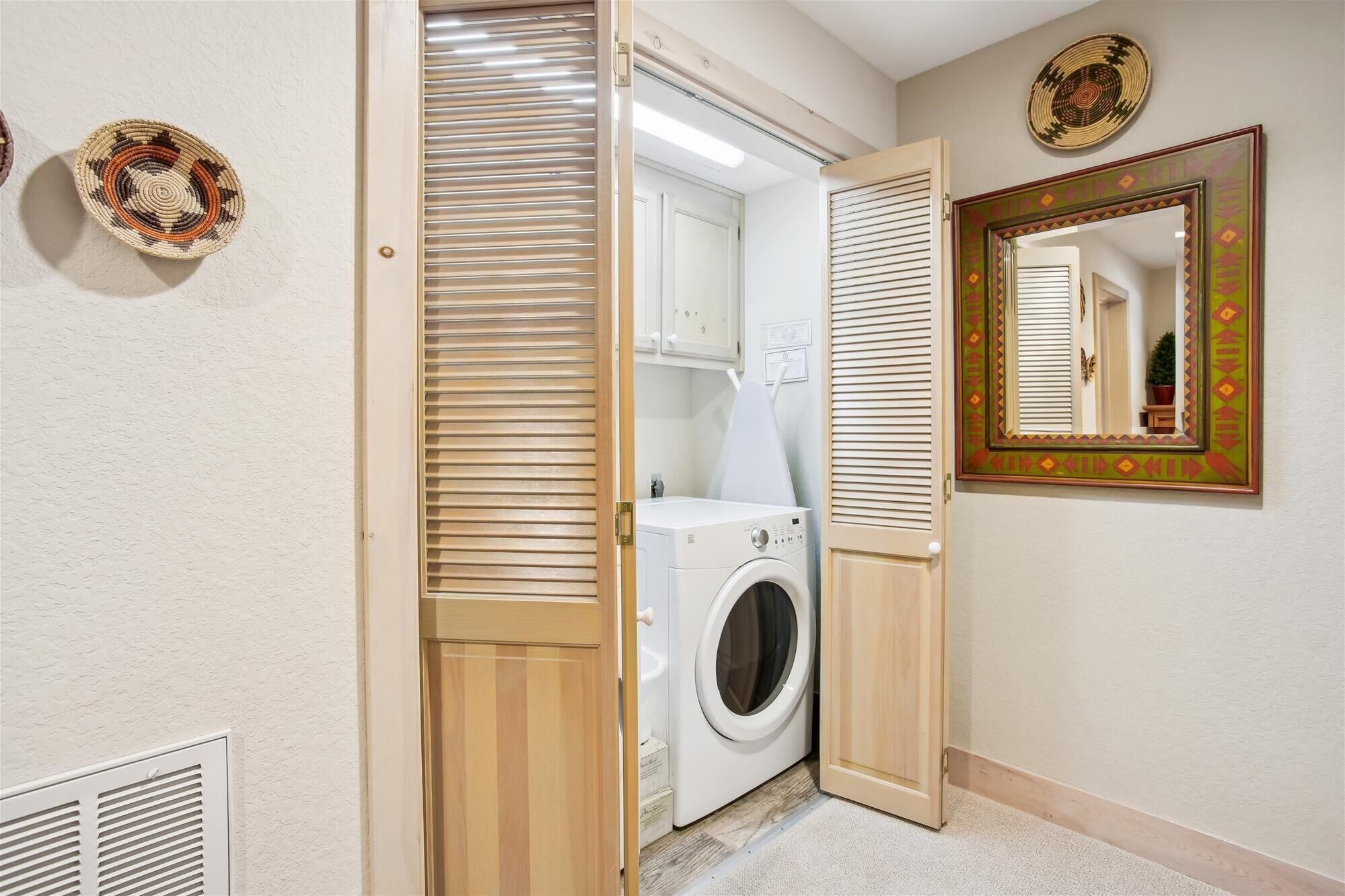 A laundry room with a washing machine, a mirror with a decorative frame, and a door with a striped pattern.