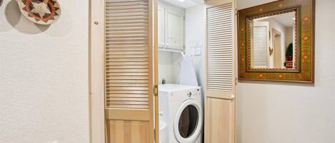 A laundry room with a washing machine, a mirror with a decorative frame, and a door with a striped pattern.