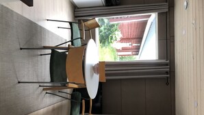 A compact room with a dining table and chairs, a window with a view of greenery and a building, and a sliding door.