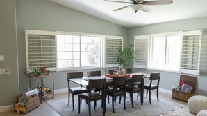 Ein Essbereich mit Tisch und Stühlen, einem Deckenventilator und einem Fenster mit Jalousien.