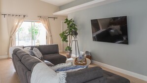 Ein Wohnzimmer mit grauem Ecksofa, einem flachbildfernseher an der Wand und einer Topfpflanze.