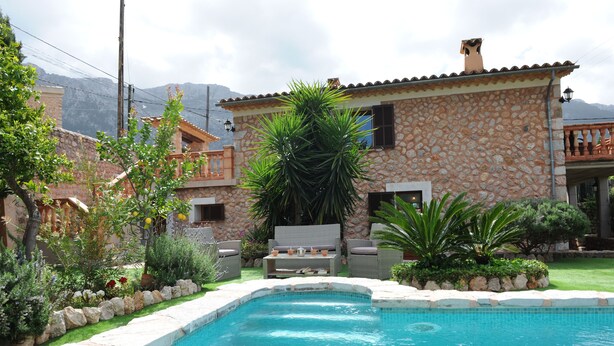 Una casa de piedra con piscina, mobiliario de exterior y jardín.