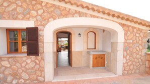 Edificio de piedra con entrada de tejas, contraventanas de madera y una pequeña cocina.