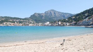 Una playa con aguas cristalinas, una montaña al fondo y edificios a lo largo de la costa.