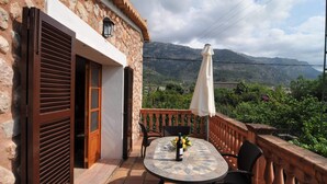 Un edificio de piedra con un balcón, una mesa con sillas y una botella de vino.