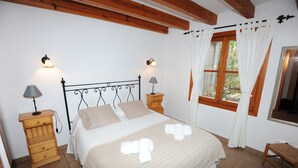 Una cama bien hecha con sábanas y toallas blancas, dos mesitas de noche con lámparas, una ventana con cortinas y un cabecero de madera.