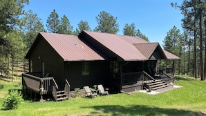 Une cabane dotée d’un porche et d’une petite terrasse, entourée d’une pelouse et d’arbres.