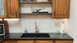 Une cuisine avec des meubles en bois, un plan de travail noir, un évier en acier inoxydable et un pare-feu décoré de carreaux hexagonaux.