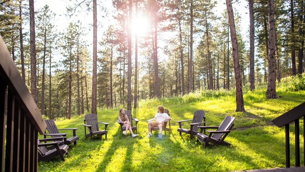 Une terrasse avec quatre fauteuils Adirondack donnant sur une forêt.