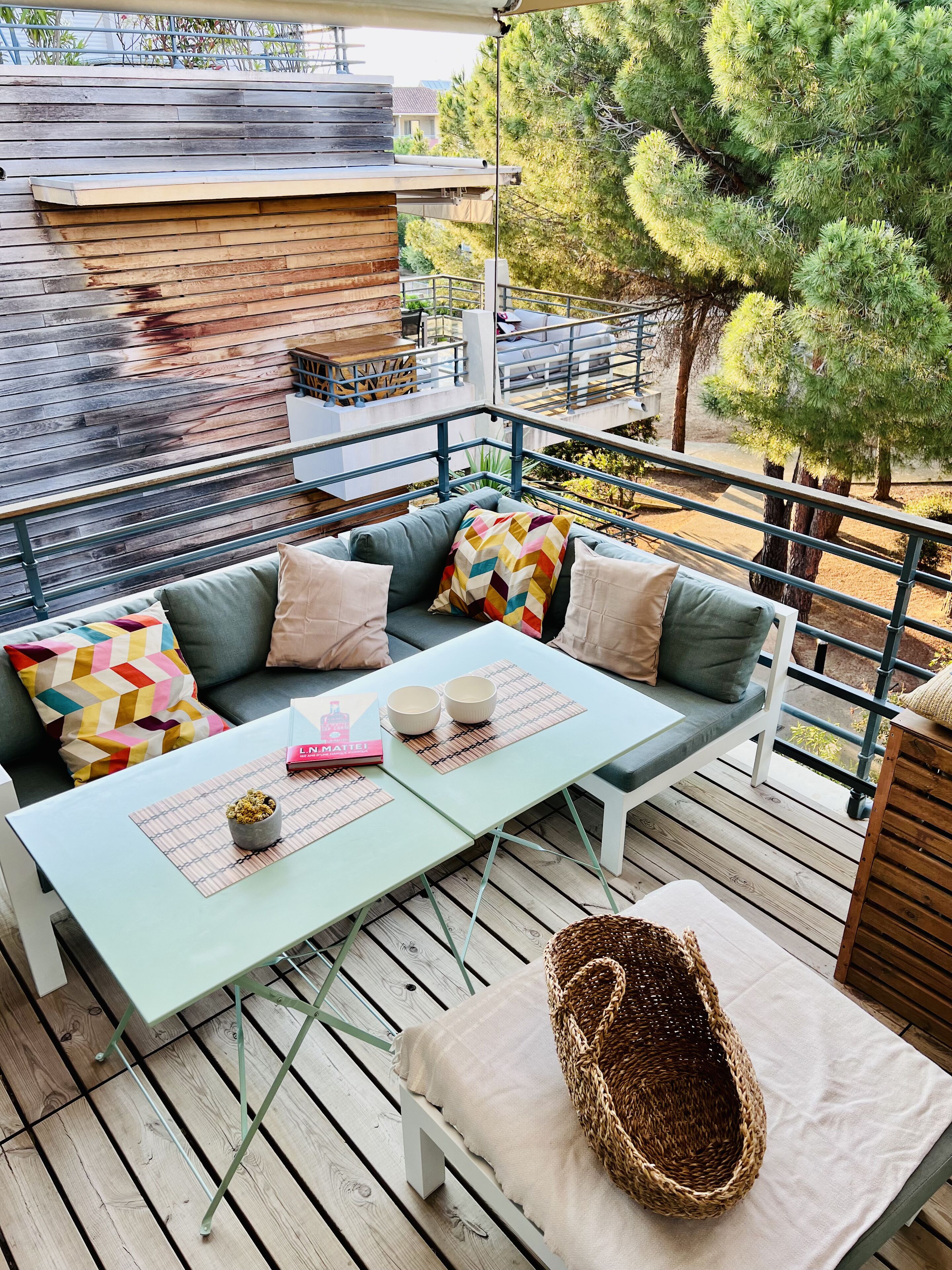 A cozy outdoor seating area with a sofa, cushions, and a table with two bowls and a book.