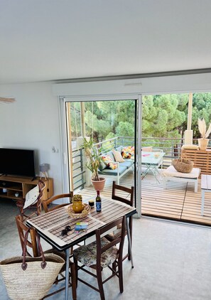 En moderne stue med fjernsyn, spisebord med stole, sofa og balkon med udendørs møbler.