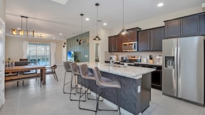 A modern kitchen with dark cabinets, stainless steel appliances, and a central island with bar stools. - Exquisite, Spacious and Close to Disney 6 BD Home #6ws483 (Kissimmee)