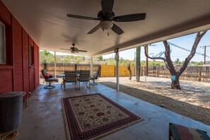 Une terrasse couverte avec des ventilateurs de plafond, une table avec des chaises et un tapis décoratif.