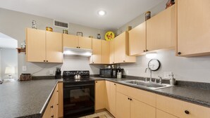 A kitchen with wooden cabinets, a black stove, a microwave, and a sink.