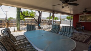 A covered patio with a pool table, striped chairs, ceiling fans, and a view of a fenced backyard.