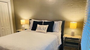 A neatly made bed with a pillow that reads "GUEST" and two bedside lamps.