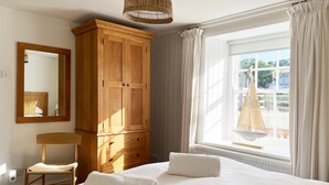 Un dormitorio con una cama grande, un armario de madera, una silla, un espejo y una ventana con cortinas.