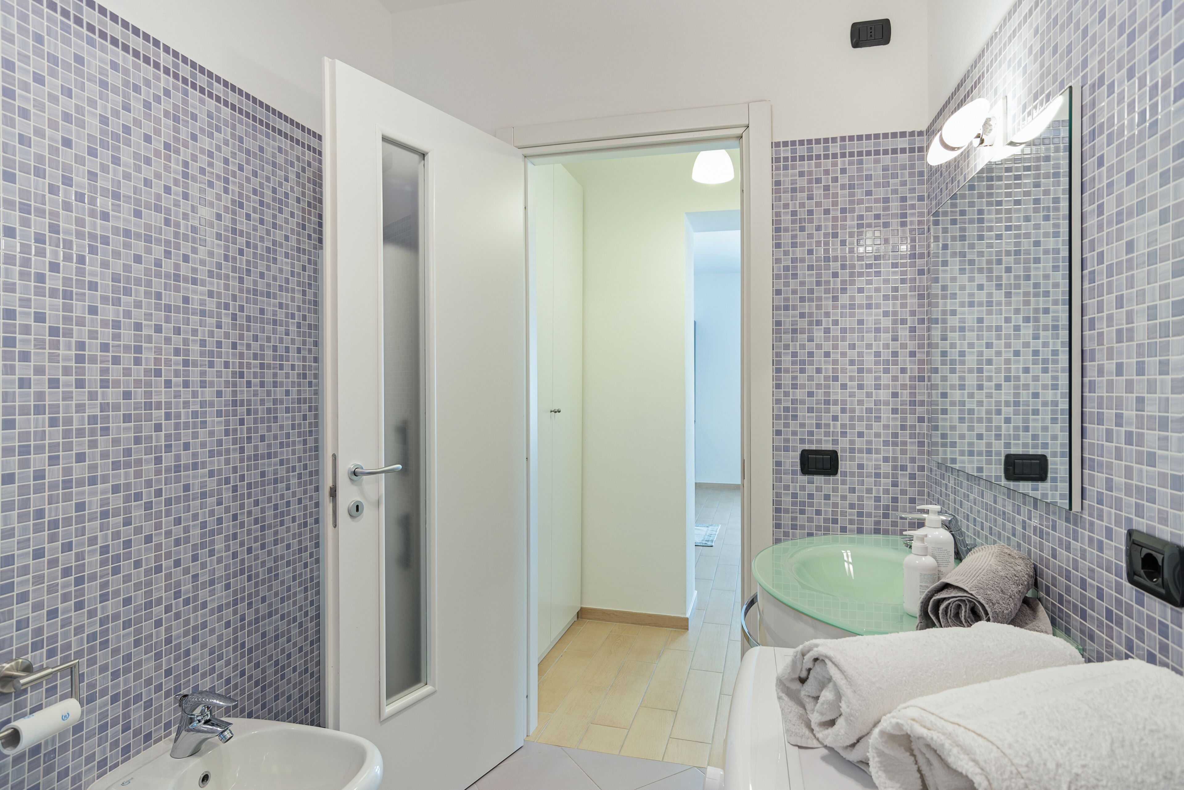 Un baño con cabina de ducha de vidrio, lavamanos con espejo y toallas en un perchero.