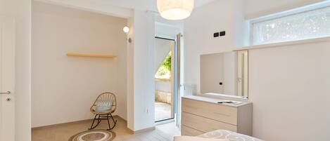 A bedroom with a bed, a bedside table, a mirror, and a door leading to a balcony.