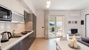 A modern kitchen with a sink, stove, and microwave. There is a dining area with a table and candles. A TV is visible in the background. - Ossuccio Island View - MyHomeInComo (Tremezzina)