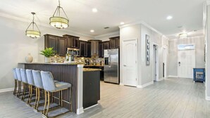 A modern kitchen with dark wood cabinets, stainless steel appliances, and a central island with bar stools. - 8BR Villa w/ Private Pool | Theater |Themed BRs (Davenport)