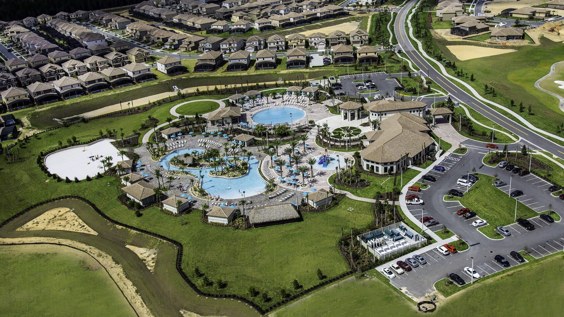 Vista aérea de un complejo turístico con múltiples piscinas, un campo de golf y un estacionamiento.