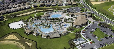 An aerial view of a resort with multiple swimming pools, a golf course, and a parking area.