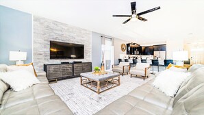Una sala de estar moderna con un televisor grande, asientos cómodos, un comedor y una cocina.