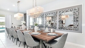 A modern dining room with a wooden table set for six, grey upholstered chairs, and a large mirror with geometric patterns on the wall. - 9BR/Star Wars/HarryPotter Themed Rooms/Pool/Disney (Davenport)