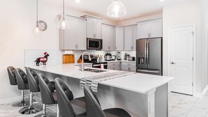 A modern kitchen with white cabinets, stainless steel appliances, and a central island with bar stools. - Avatar Game Room + Harry Potter BR w/ Pool~Spa (Kissimmee)
