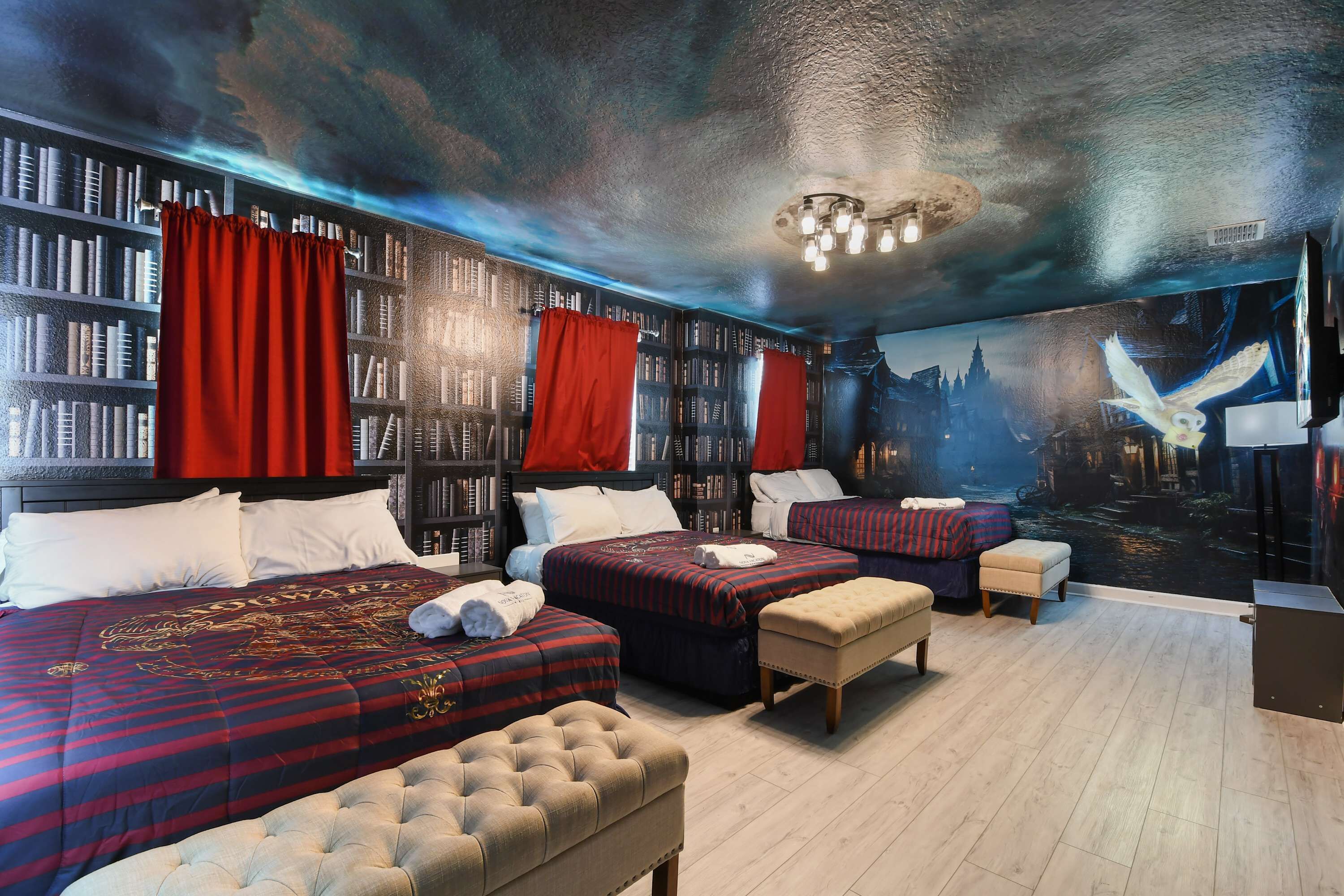 Ein Hotelzimmer mit zwei Betten, einem großen Bücherregal und einem Wandgemälde einer Stadtansicht.