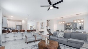 Ein modernes Wohnzimmer mit grauem Sofa, einem Couchtisch und einer Küchenzeile mit weißen Schränken und einem Kühlschrank.