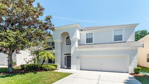 A two-story house with a garage, a front entrance with a door, and a tree in the front yard. - Close2Parks, 7BR, Themed room @ Windsor Hill! (Kissimmee)