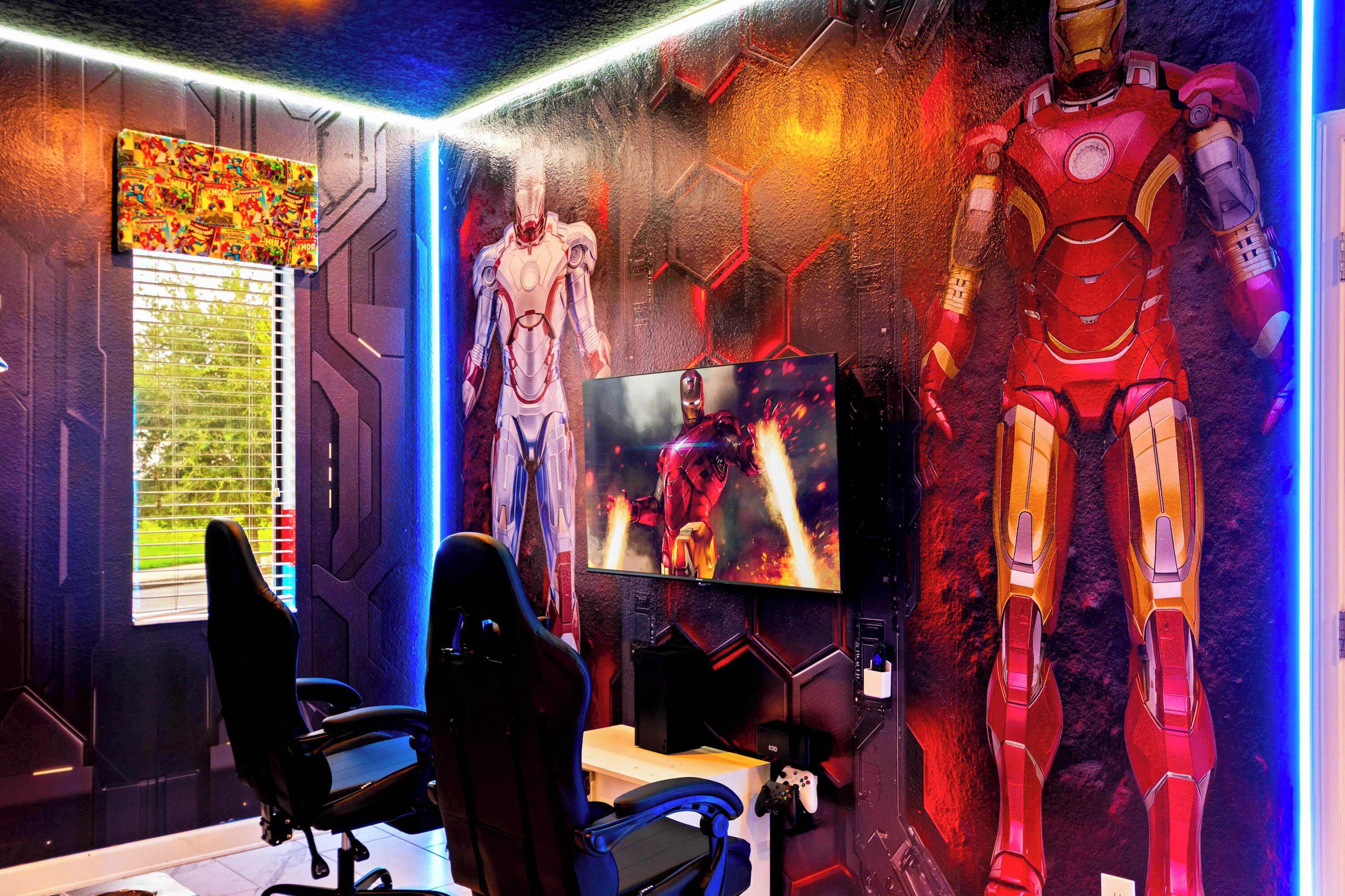 A gaming room with two gaming chairs, a TV, and two large Iron Man statues.