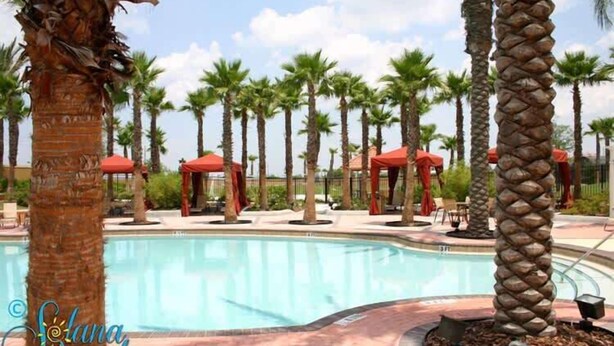 A swimming pool surrounded by palm trees and red umbrellas.